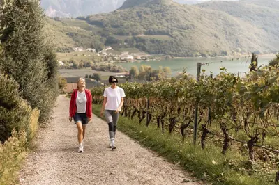 two women walking down a path through a vineyard at Lake Spa Hotel SEELEITEN in Caldaro