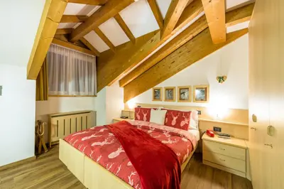 a bedroom with a red bed and wooden ceilings at Alpstyle Hotel Albolina Wellness & Beauty in Canazei