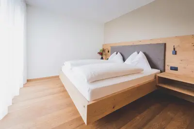 a bedroom with a white bed with a wooden headboard at Sinnergut in Nalles