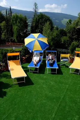 a group of chairs with an umbrella on the grass at Hotel Klammer in Vipiteno