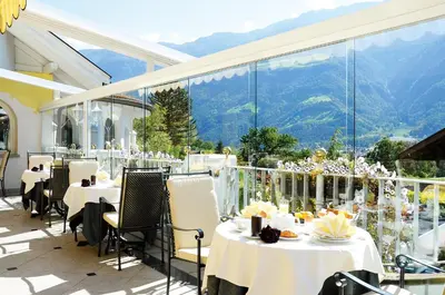 a restaurant with tables and chairs with mountains in the background at Hotel Funggashof in Naturno