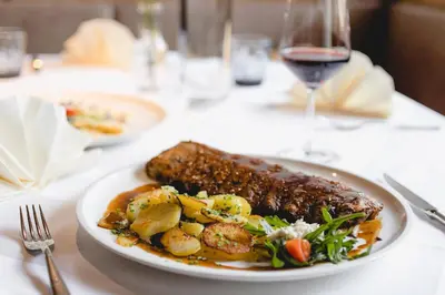 a plate of meat and vegetables on a table with a glass of wine at Hotel Schmuckhof in Chiusa