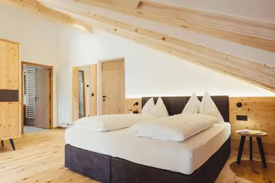 a bedroom with a large white bed with wooden ceilings at Hotel Schmuckhof in Chiusa