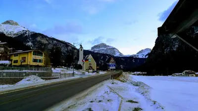 a snowy road with a church and mountains in the background at CasaMau Studio in Campitello