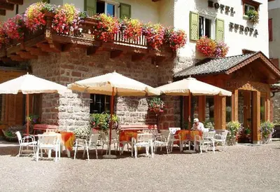 an outdoor cafe with tables and chairs and umbrellas at Hotel Europa in Moena