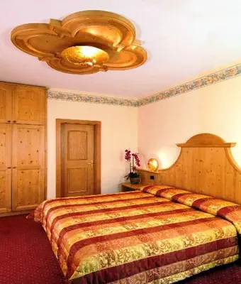 a bedroom with a large bed and a chandelier at Hotel Europa in Moena