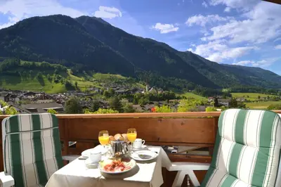 a table with a plate of food on a balcony with mountains at Residence Talblick in San Leonardo in Passiria