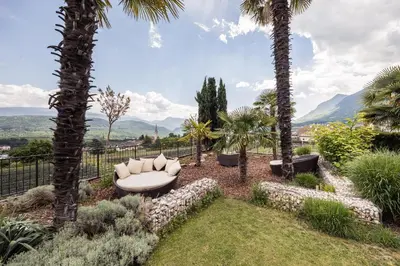 a white couch sitting in a garden with palm trees at Felderer Boutiquehotel B&B in Caldaro