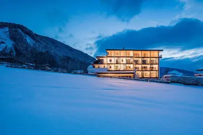 a large building next to a snow covered lake at Hotel Mühlgarten in San Lorenzo di Sebato