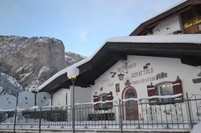 a building covered in snow with a mountain in the background at Hotel Scoiattolo in Selva di Val Gardena