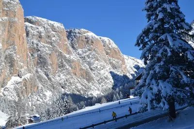 a group of people walking in the snow next to a mountain at Hotel Scoiattolo in Selva di Val Gardena