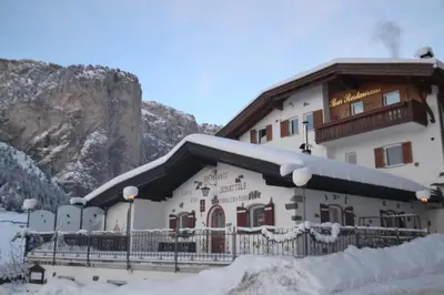 a building covered in snow in front of a mountain at Hotel Scoiattolo in Selva di Val Gardena