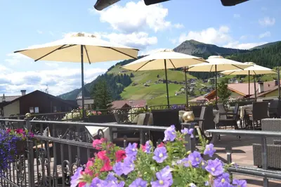 a patio with tables and umbrellas and flowers at Hotel Scoiattolo in Selva di Val Gardena