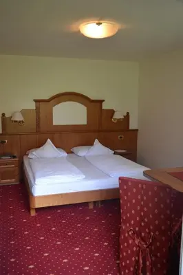 a bedroom with a large bed and a chair at Hotel Scoiattolo in Selva di Val Gardena