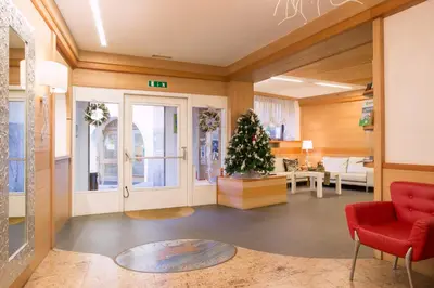 a living room with a christmas tree and a red chair at Hotel Al Cervo in Tesero