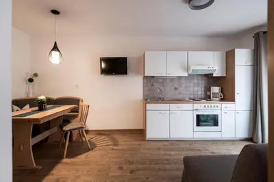 a kitchen with white cabinets and a wooden table with a dining room at Garni Grünau in San Martino