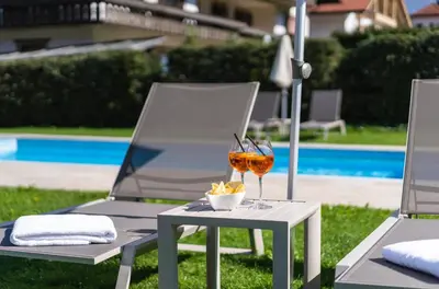a table with a glass of wine and two chairs at Hotel Reischach in Brunico