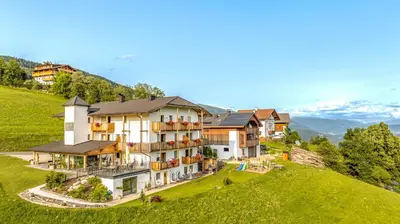 a building on top of a hill with mountains in the background at Hotel Pfeiferhof in Maranza