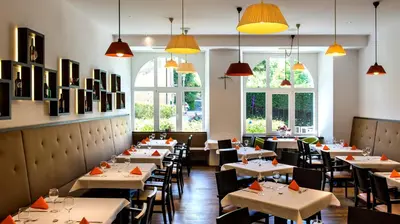 a restaurant with white tables and chairs and windows at Hotel Kolping in Merano