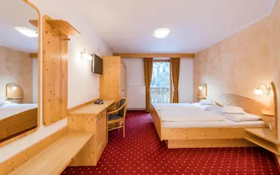 a hotel room with two beds and a desk at B&B Hotel Alpenrose Rooms & Apartments in Valles