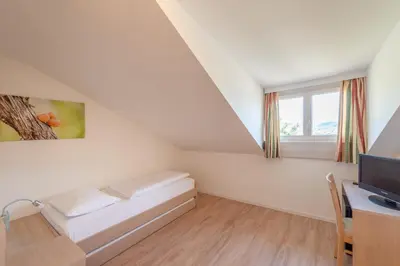 a small white room with a bed and a desk at Garni Hotel Ritterhof in Termeno