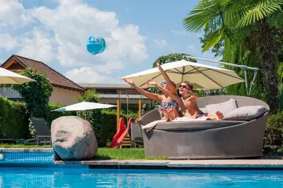 two women in bathing suits are sitting on a pool at Hotel Spitaler in Appiano sulla Strada del Vino