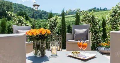 a table with a vase of orange flowers and glasses at Hotel Spitaler in Appiano sulla Strada del Vino