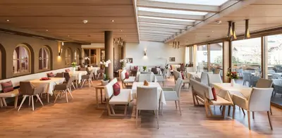 a restaurant with white tables and chairs and windows at Hotel Spitaler in Appiano sulla Strada del Vino
