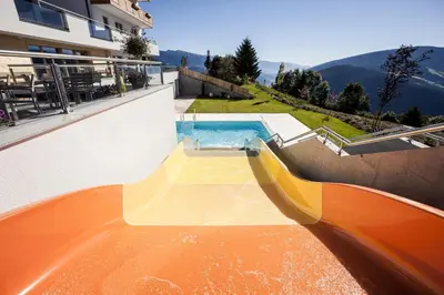 a swimming pool with a slide next to a building at Family Home Alpenhof in Maranza