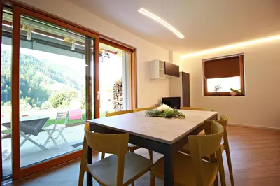 a dining room with a table and chairs and a large window at casa waldner in Castello di Fiemme