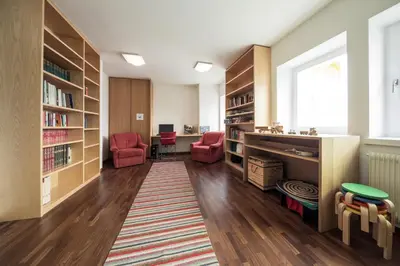 a library with bookshelves and red chairs in a room at Hotel Masatsch in Caldaro