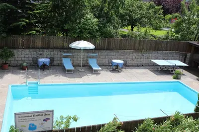 a swimming pool with tables and chairs and an umbrella at Gasthof Anny in Marlengo