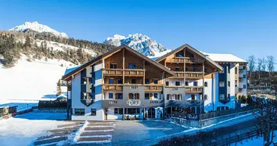 a large building in the snow with mountains in the background at Residence Rautal B&B ***S in San Vigilio Di Marebbe