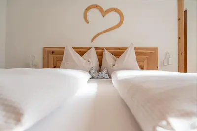 two beds with white sheets and a heart on the wall at Schweinsteghof Urlaub auf dem Bauernhof in Sarntal