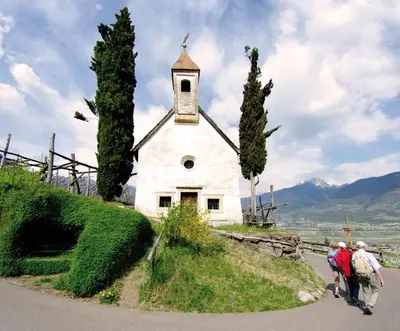 a group of people walking past a small white church at Appartements Peilerhof in Cermes