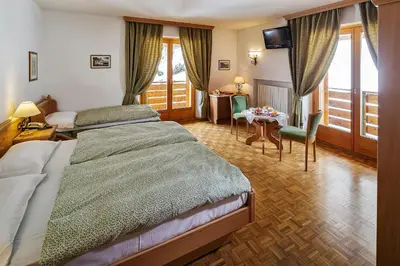 a hotel room with two beds and a table and chairs at Hotel Piccolo Pocol in Cortina dʼAmpezzo