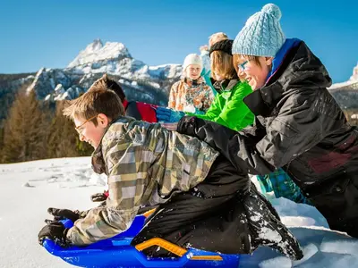 a group of people playing in the snow on a snowboard at Hotel Piccolo Pocol in Cortina dʼAmpezzo