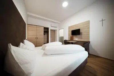 two beds in a hotel room with a cross on the wall at Kolpinghaus Bolzano in Bolzano