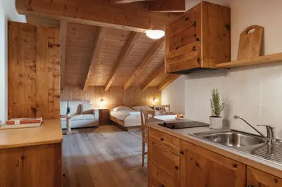 a kitchen with wooden cabinets and a living room at Garni Ciasa Urban in Badia