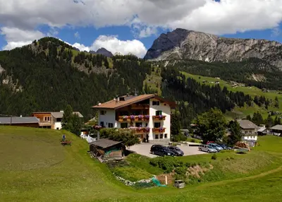 a building on a hill with mountains in the background at Villa Insam Apartment in Selva di Val Gardena