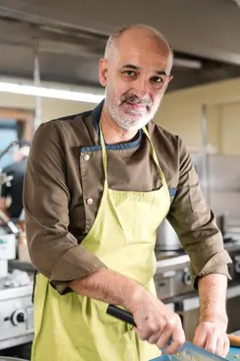 a man wearing an apron preparing food in a kitchen at Al Plan, A mountain moving hotel in San Vigilio Di Marebbe