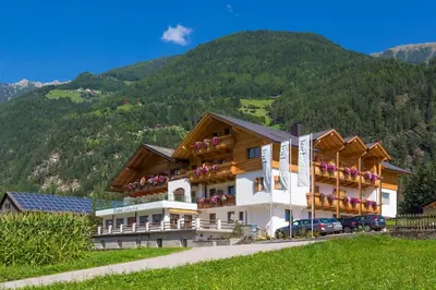 a building with flowers on the balconies in front of a mountain at Hotel Foestlerhof in Villa Ottone