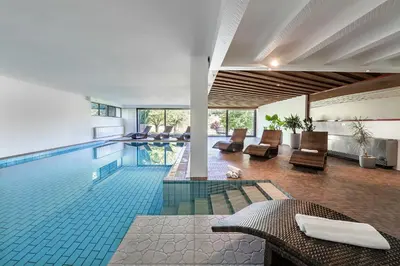 a swimming pool with chairs and a table in a building at Hotel Wiedenhofer in Terento