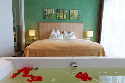 a bedroom with a bed and a bath tub with red flowers at Hotel Amaten in Brunico