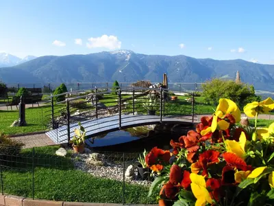 a bridge over a pond in a park with flowers at Hotel Amaten in Brunico