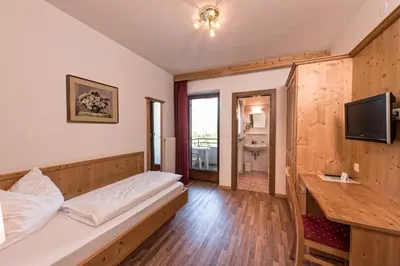 a room with two beds and a desk and a television at Hotel St. Justina Hof in Appiano sulla Strada del Vino