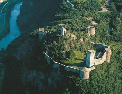 a castle on top of a mountain next to a river at Hotel St. Justina Hof in Appiano sulla Strada del Vino