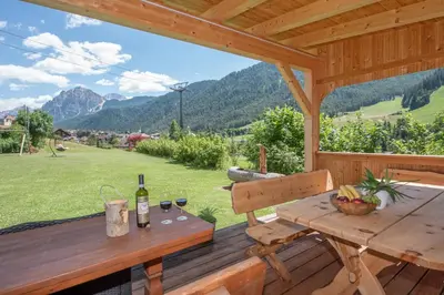 a wooden deck with a table with a bottle of wine at Villa Sole in San Vigilio Di Marebbe