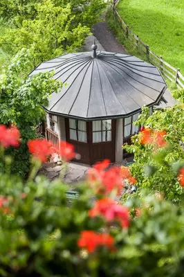 a small building with a roof in a garden with red flowers at Hotel Latemar in Soprabolzano