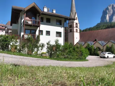 a house with a church and a car parked in front at Villa Ula Verda- Apartments Marianna in Santa Cristina in Val Gardena